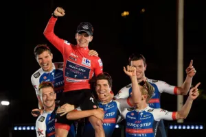 Team Quick Step's Belgian rider Remco Evenepoel (C) celebrates with teammates on the podium wearing the overall leader's red jersey after the 21st and last stage of the 2022 La Vuelta cycling tour of Spain, a 96.7km race from Las Rozas de Madrid to Madrid, on September 11, 2022. - Belgian rider Remco Evenepoel claimed his first Grand Tour victory in the Vuelta a Espana in Madrid. The 22-year-old dominated the three-week race, taking victory after the 21st and final stage won by Colombian Juan Sebastian Molano. (Photo by OSCAR DEL POZO / AFP)