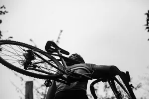 greyscale photography of man carrying cyclocross bike