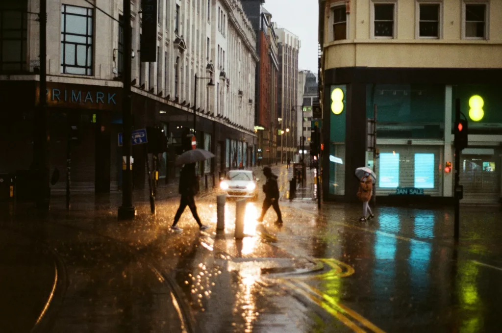 a group of people walking across a street holding umbrellas wet roads